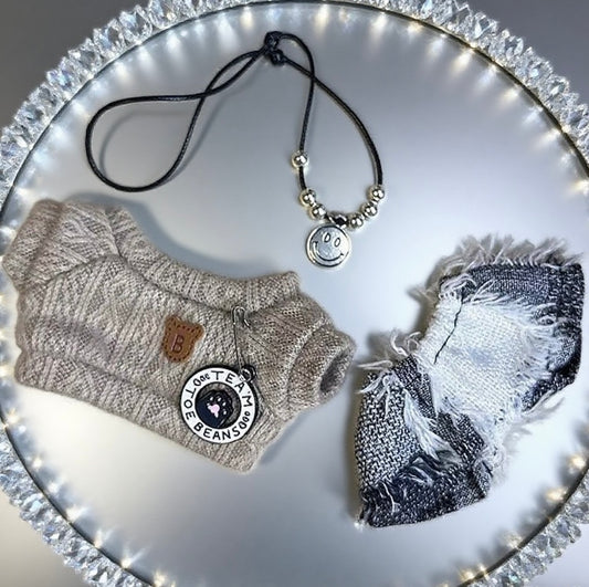 Labubu dolls clothes including a sweater, scarf, and necklace on a decorative plate with lights.