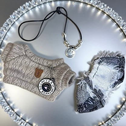 Labubu dolls clothes including a sweater, scarf, and necklace on a decorative plate with lights.